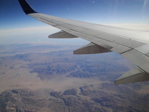 1989 Ford Taurus - View from an airplane window shows a wing extending over a vast, arid landscape with mountains and valleys below.