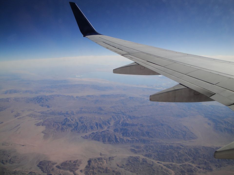 Airplane wing in foreground, desert mountains below