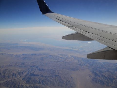 1989 Ford Taurus - Aerial view of arid terrain with mountains and a body of water in the distance, seen from an aircraft.