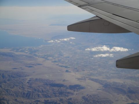 1989 Ford Taurus - View from an airplane window shows a wing extending over a vast desert landscape and a distant coastline.