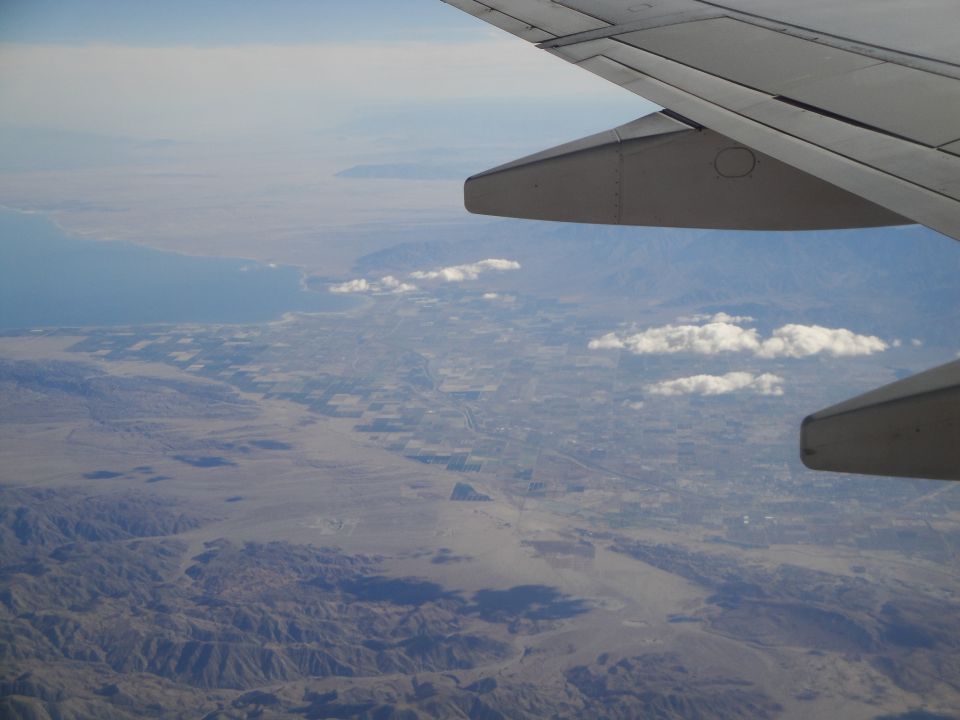 Airplane wing over a desert landscape with a body of water in the distance