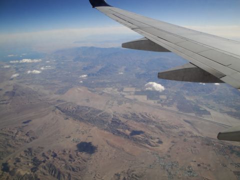 1989 Ford Taurus - View from an airplane window shows a wing extending over a vast desert terrain with distant mountains under a clear blue sky.