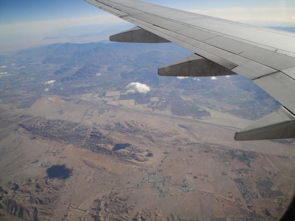Airplane wing over arid landscape with mountains and a highway