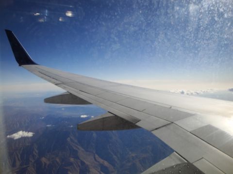 1989 Ford Taurus - View from an airplane window shows the wing and the mountainous terrain below under a clear blue sky.