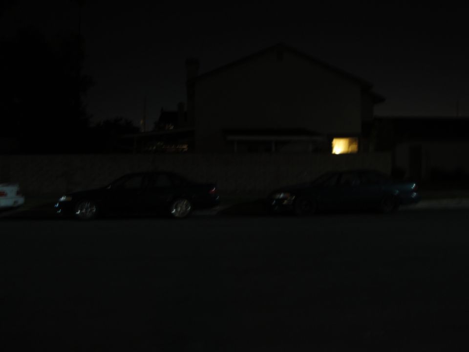 Two sedans parked on a street at night in front of a house