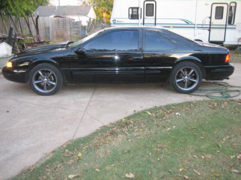 1996 Ford Thunderbird - Side profile of a black 1996 Ford Thunderbird coupe with aftermarket wheels and hood scoop.
