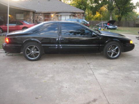 1996 Ford Thunderbird - Side view of a black 1996 Ford Thunderbird parked in front of a house.