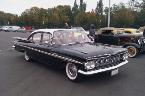 1991 Ford LTD Crown Victoria - A classic black 1959 Chevrolet Impala with distinctive tail fins is parked outdoors.