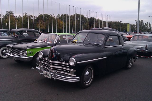 Black coupe with pinstripes on hood, parked next to a green and black car. License plate visible
