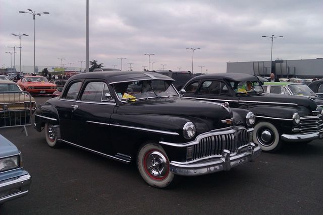 Two black sedans parked side-by-side, one in foreground with chrome grille and red-rimmed wheels