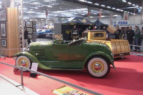1991 Ford LTD Crown Victoria - A green roadster with whitewall tires is displayed on a red carpet next to a wooden-bed truck.