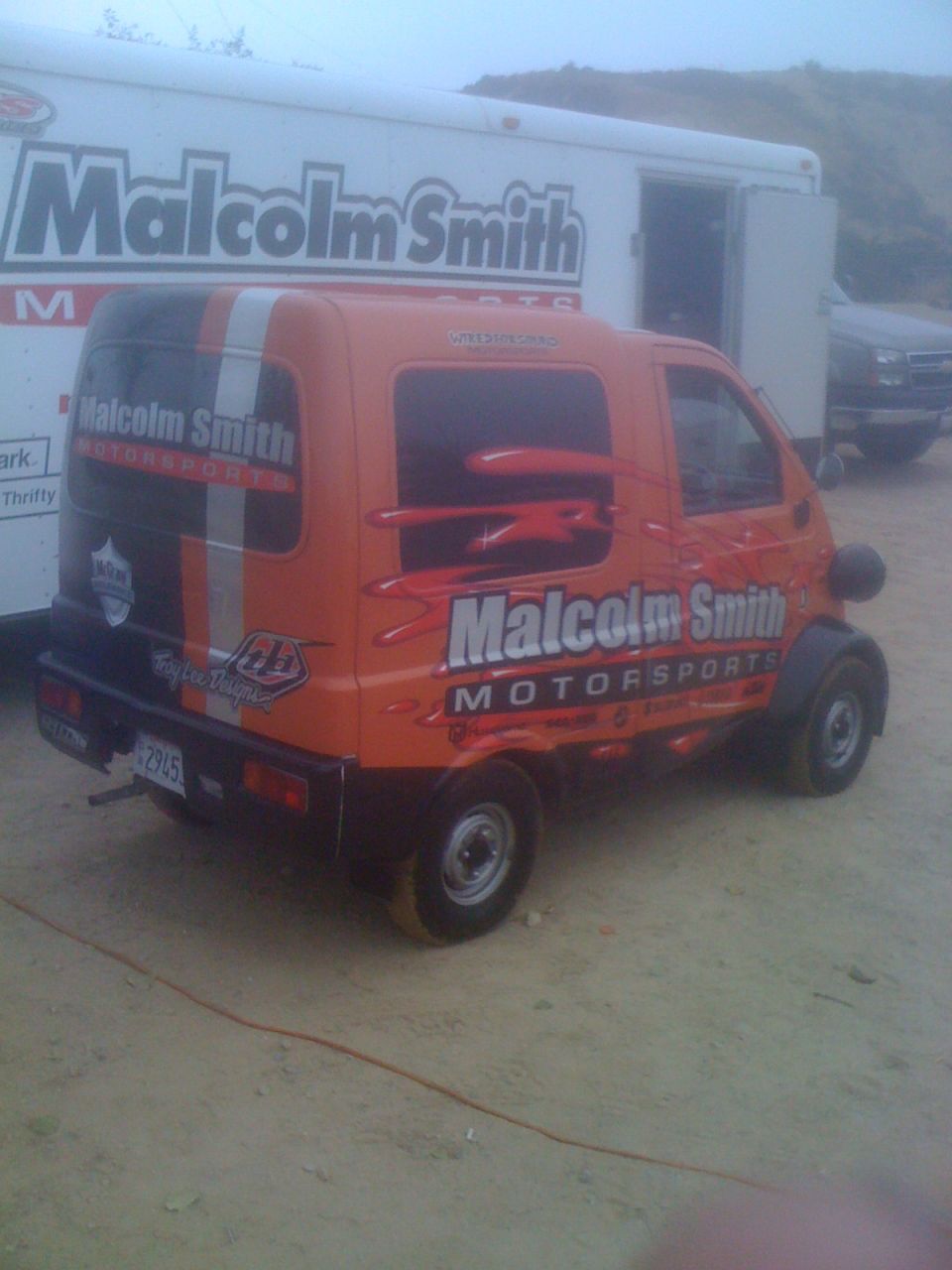 Orange van with Malcolm Smith Motorsports livery parked next to a white trailer