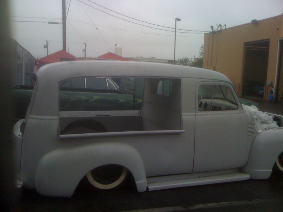Gray panel truck with custom window cutouts, lowered suspension, and white-rimmed tires