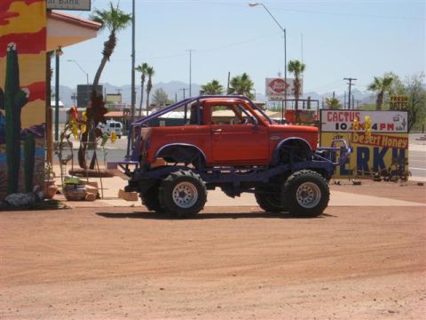 1968 Ford Mustang - Modified truck with oversized tires and custom roll cage sits in a dusty lot.