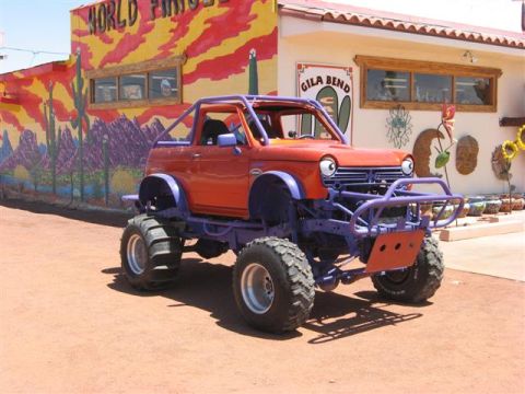 1968 Ford Mustang - A heavily modified vehicle with large tires and a custom front bumper sits outside a building decorated with a vibrant desert mural.