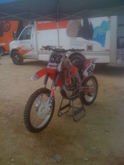 1968 Ford Mustang - A dirt bike with the number 153 is parked on a stand in front of a white truck.