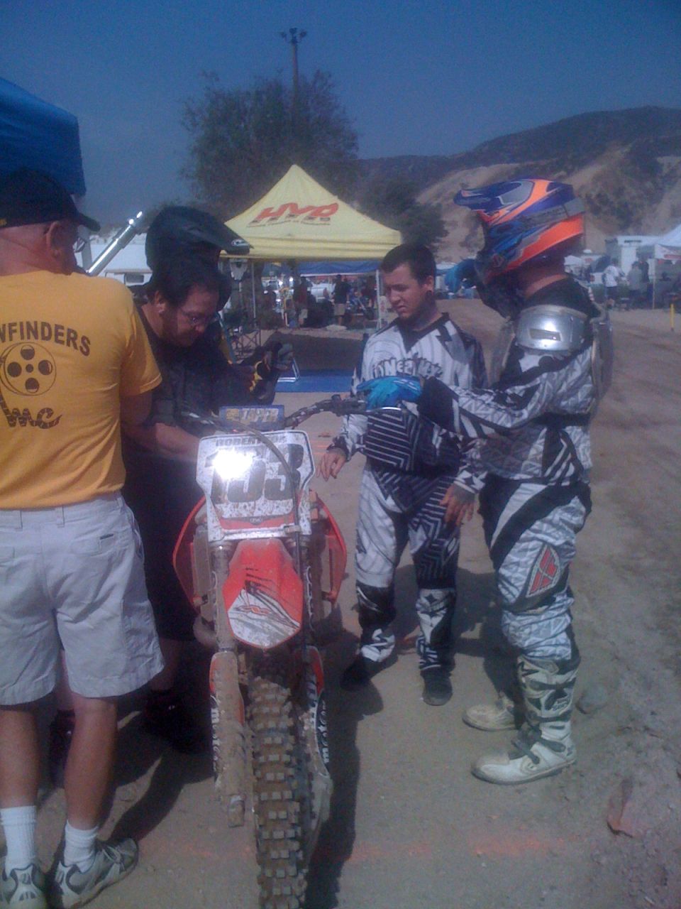 Motocross riders gathered around a dirt bike with number 33 on the front
