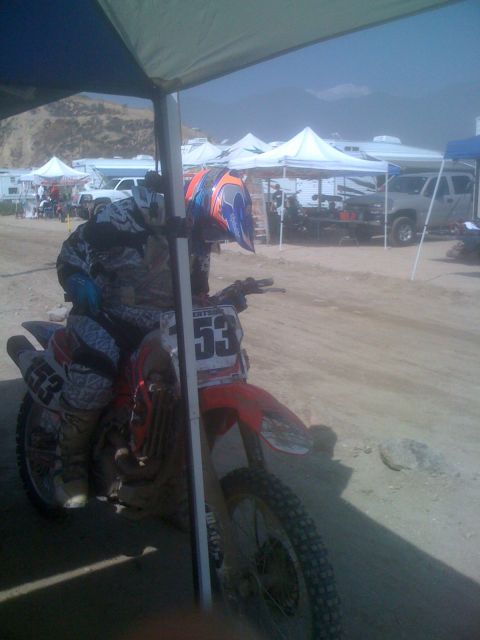 1968 Ford Mustang - A motocross rider and their bike are parked under a canopy at an outdoor event, with other tents and vehicles visible in the distance.