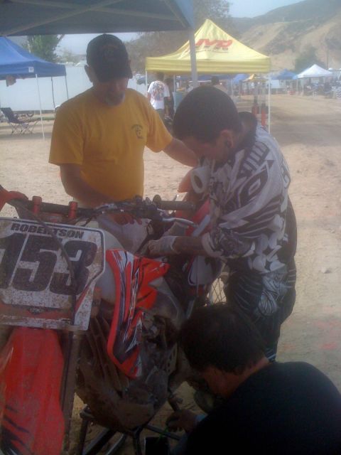 1968 Ford Mustang - Mechanics attend to a motocross bike at an event, with tents and hills in the background.