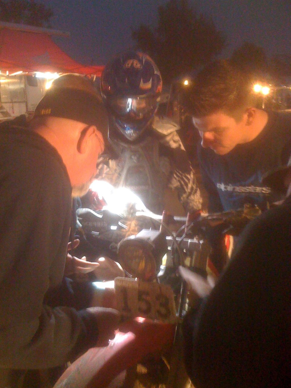Motorcycle with number 153 on a plate, surrounded by people at dusk
