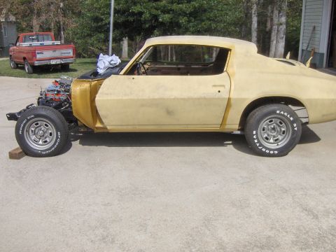 1970 Chevrolet Camaro - A car body in primer is shown with its engine exposed, while a red pickup truck sits in the background.