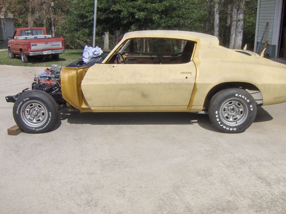 car body in primer, engine out front, red pickup truck in background