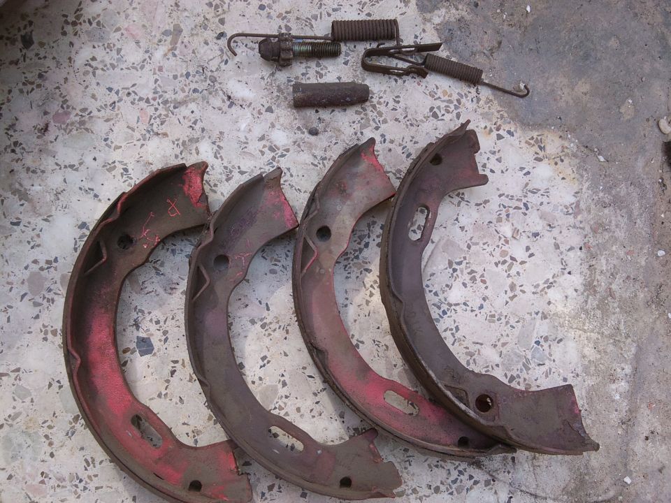 Four old brake shoes and some springs laid out on a concrete surface
