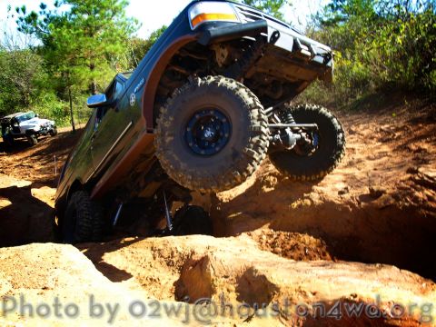 1995 Ford Bronco - A dark Ford Bronco navigates a challenging off-road course, with a white SUV in the background.