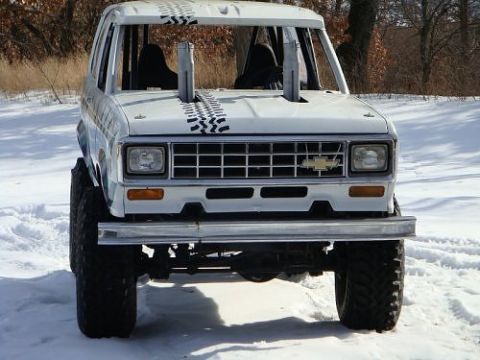 1991 Ford Bronco - Head-on front view of a stripped white 1980s Ford Bronco trail rig sitting in deep snow, with the windshield removed, an exposed roll cage,…