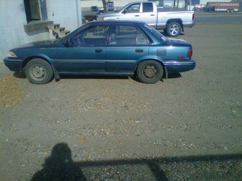 1994 Ford F-150 - A teal sedan is parked on a gravel lot next to a silver pickup truck.