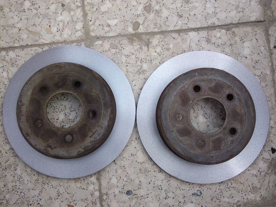 Two brake rotors, one new and one used, on a concrete surface