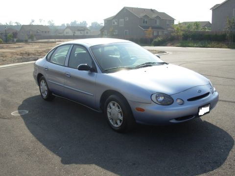 1997 Ford Taurus - A light blue 1997 Ford Taurus is parked on a street in front of a residential area.