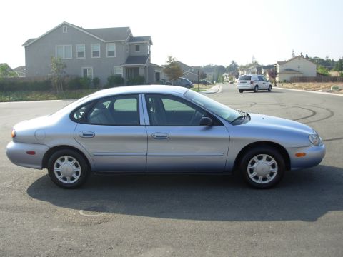 1997 Ford Taurus - A silver sedan is parked on a street with houses and a white minivan in the distance.