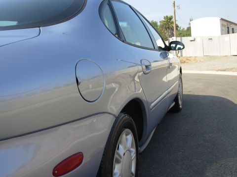 1997 Ford Taurus - The rear passenger side of a silver sedan is shown parked outdoors on a sunny day.