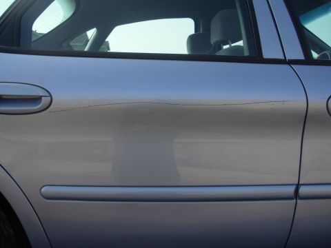 1997 Ford Taurus - A silver sedan's side door shows damage, including a noticeable dent and a scratch.