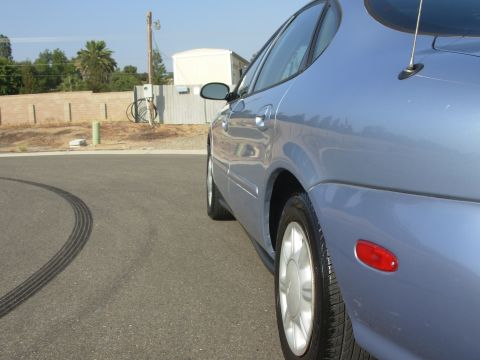 1997 Ford Taurus - Side view of a blue 1997 Ford Taurus sedan with tire marks on the road.