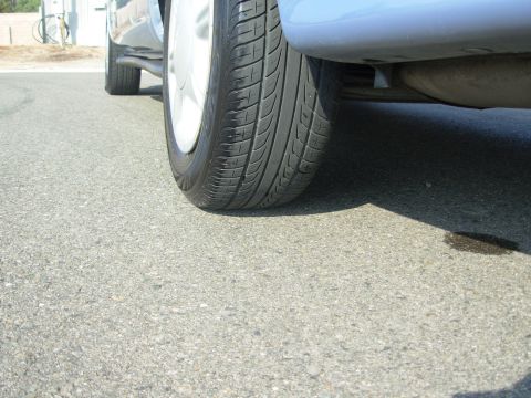 1997 Ford Taurus - A close-up view of a car's tire and undercarriage, with a dark fluid stain on the asphalt below.