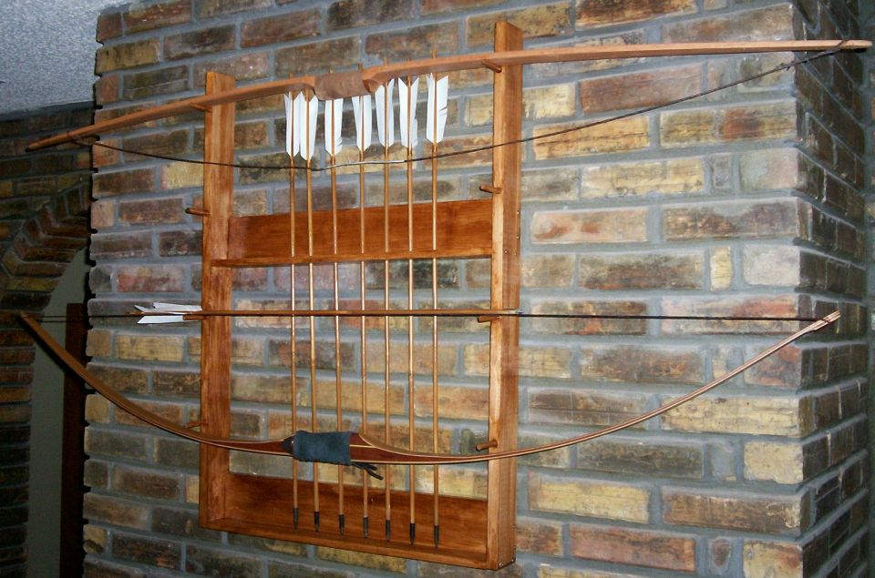 Wooden wall rack on brick holding two bows and wood arrows with white fletching