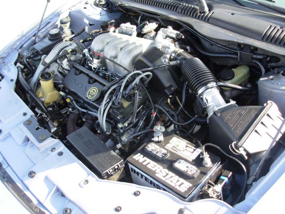 Engine bay of a silver Ford with 3.0L V6 and Interstate battery