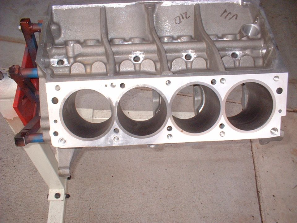 Aluminum engine block with four cylinders visible, mounted on a stand