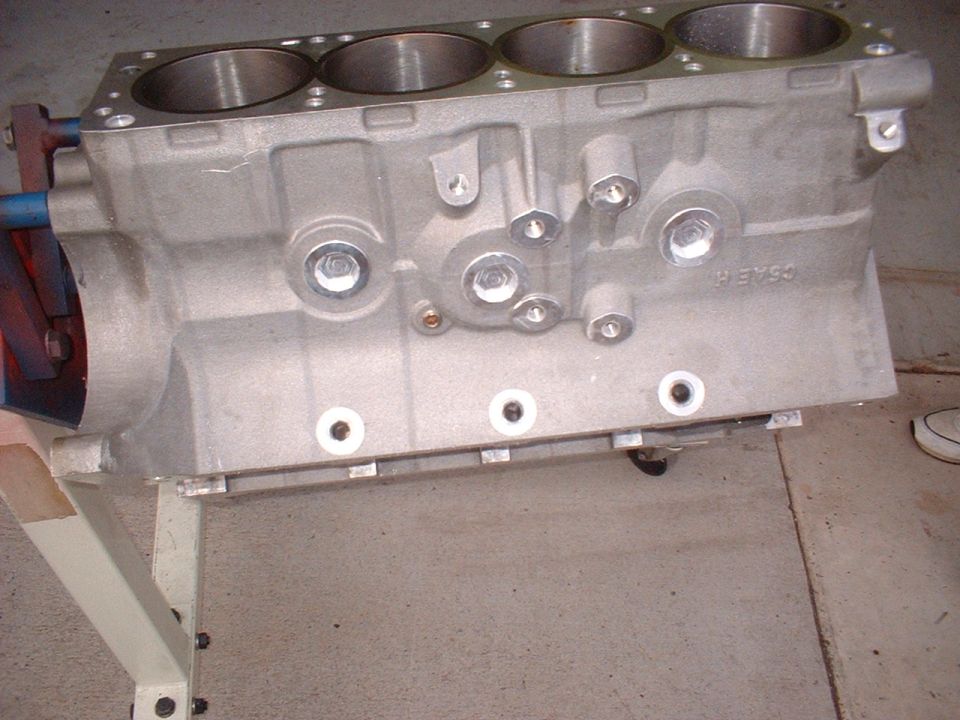 Aluminum engine block with four cylinders visible, mounted on a stand