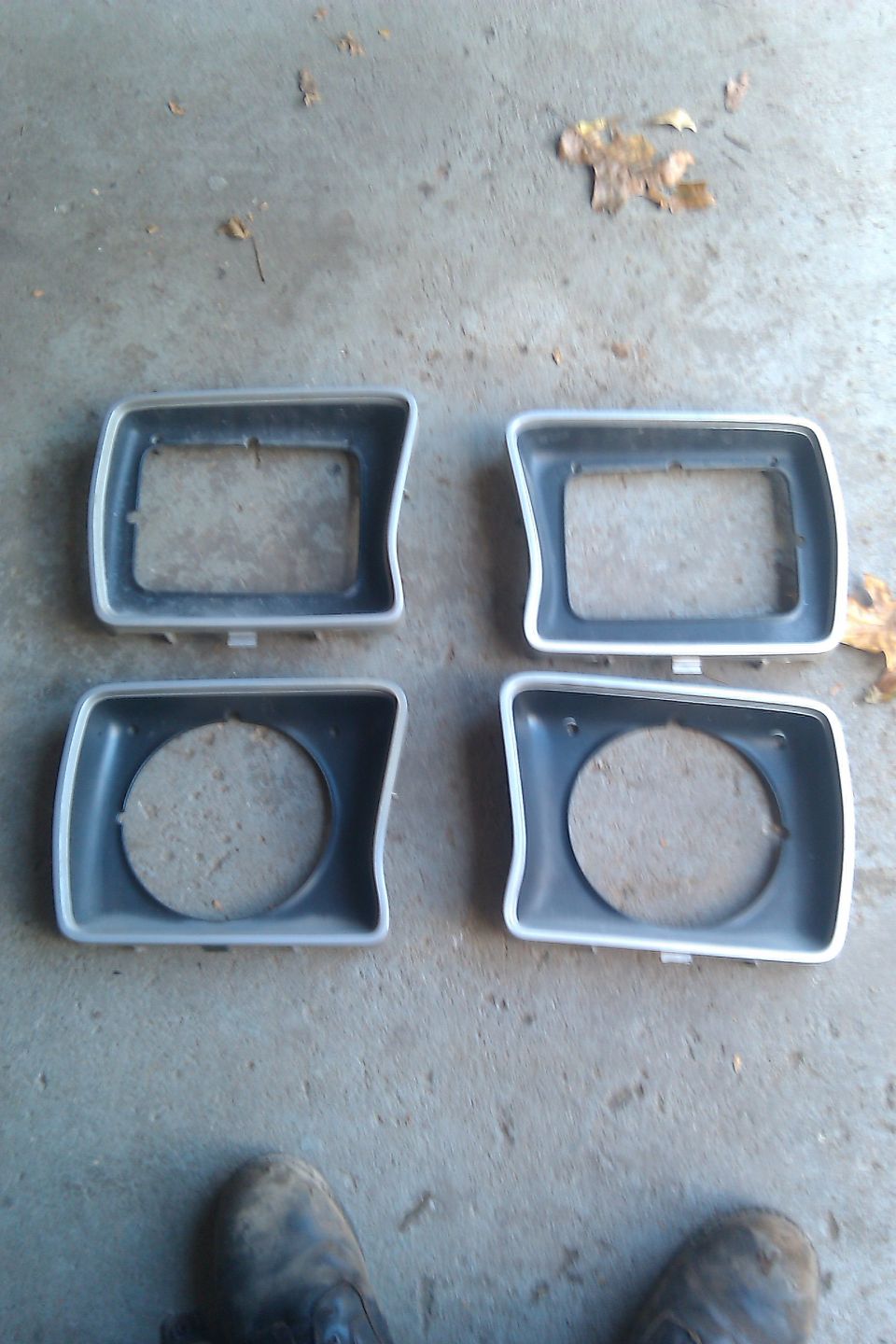 Four headlight bezels, two rectangular and two round openings, on a concrete surface