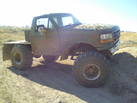1989 Ford Bronco - This heavily modified flatbed truck, likely a 1992 Ford F-Series, is covered in mud and appears to be used for off-road excursions.