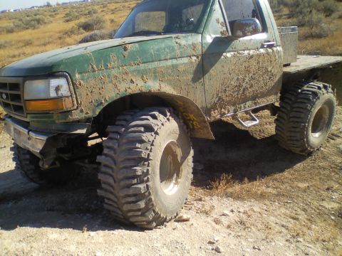1989 Ford Bronco - This heavily modified flatbed truck is covered in mud, showing off its large off-road tires.