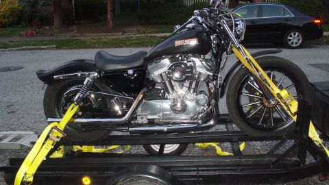 1988 Ford Bronco - Harley-Davidson motorcycle being transported on a trailer, with a black sedan in the background.