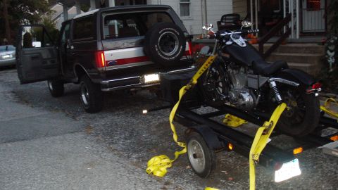 1988 Ford Bronco - A Ford Bronco is parked with its door open, hitched to a trailer carrying a motorcycle.