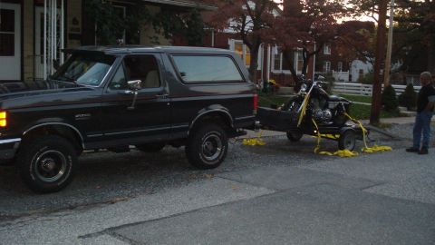 1988 Ford Bronco - A dark 1988 Ford Bronco is seen from the side, towing a motorcycle on a trailer.