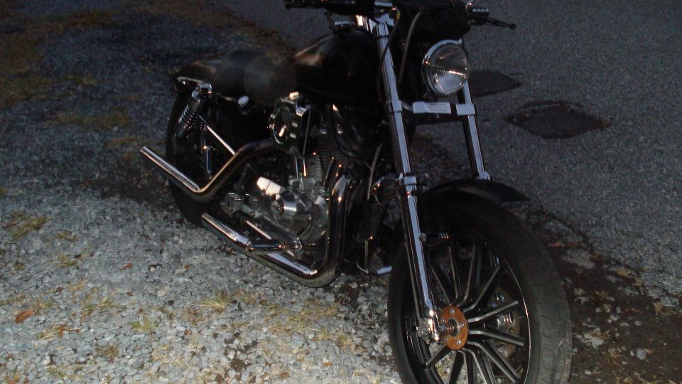 Black motorcycle with chrome exhaust and spokes parked on gravel