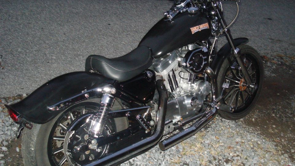 Black Harley-Davidson motorcycle parked on gravel. Shows the engine, seat, and rear wheel