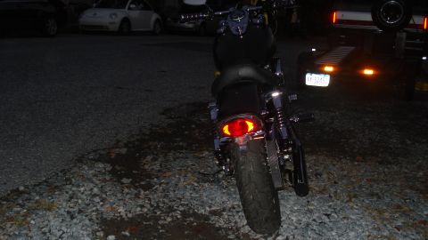 1988 Ford Bronco - A motorcycle is parked in a gravel lot at night, with a trailer visible in the background.